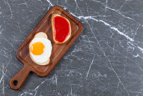 Jam and fried eggs on two slices of bread on the board , on the marble background