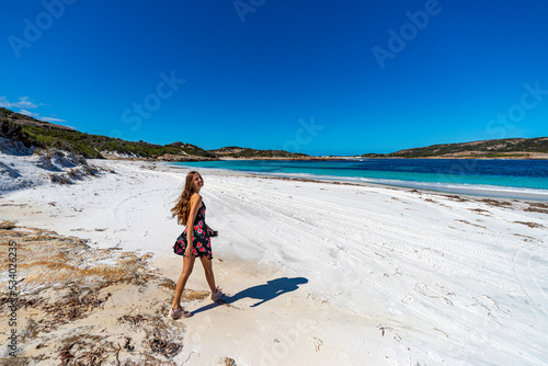 long-haired girl in a black dress with roses walks along a paradise beach with white sand and turquoise water and orange rocks, lucky bay, cape le grand national park near esperance, western australia