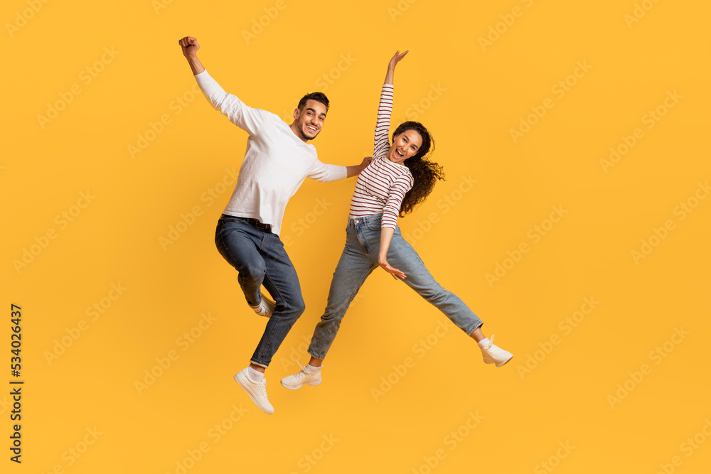Playful Mood. Happy Middle Eastern Couple Jumping In Air Over Yellow Background