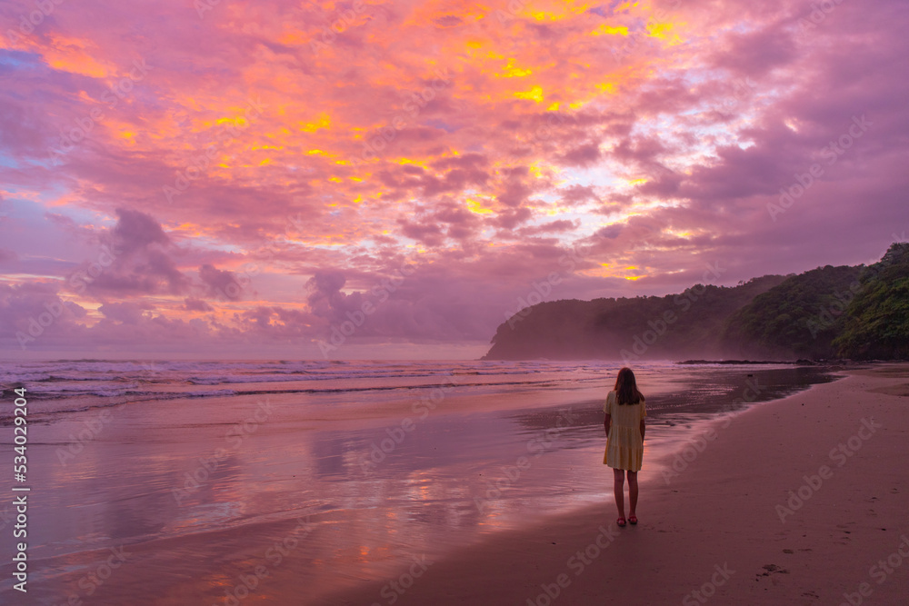 Fototapeta premium pretty girl in dress watching unique pink colorful sunset on the beach in costa rica, pacific coast - playa san miguel