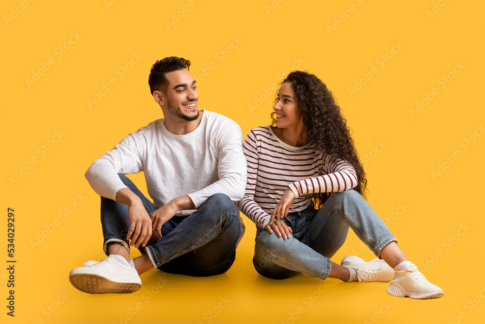Portrait of beautiful young middle eastern couple sitting together over yellow background Portrait of beautiful young middle eastern couple sitting together over yellow background