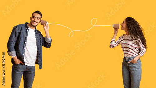 Romantic Arab Couple Communicating Through Tin Phone Over Yellow Background photo