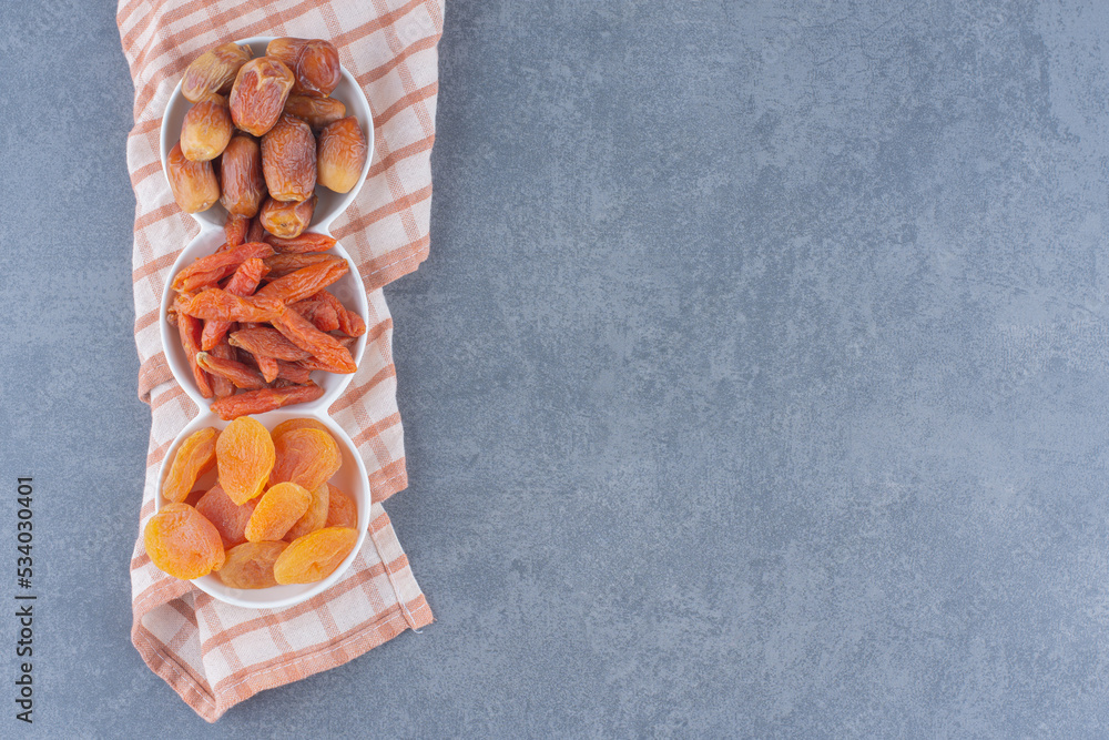 Flavorful dried fruits in bowls on the towel, on the marble background Flavorful dried fruits in bowls on the towel, on the marble background