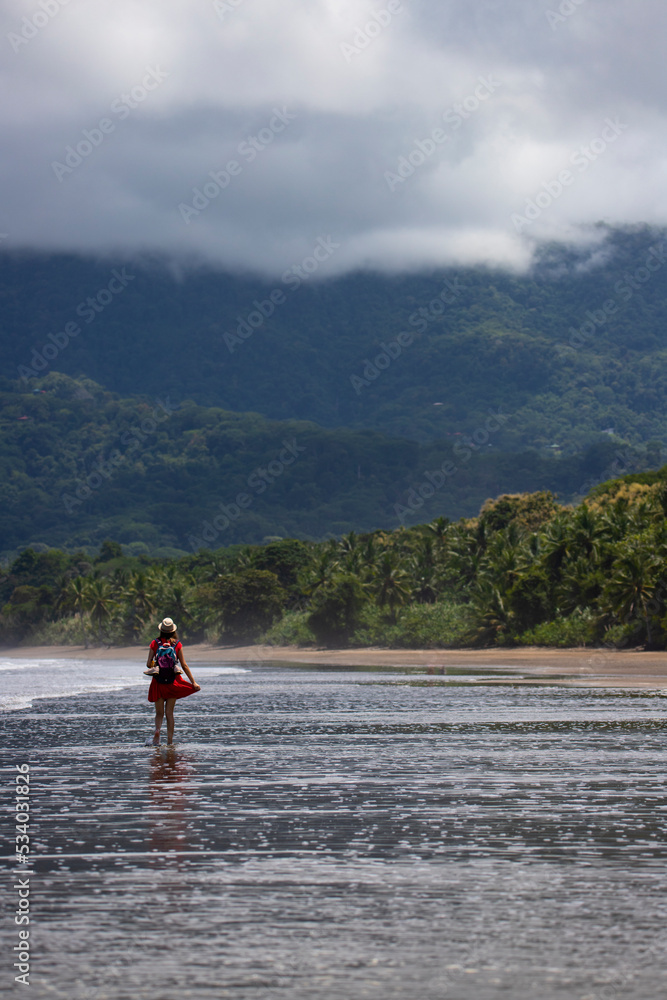 beautiful girl enjoying walk on the tropical beach with palm trees in the background; cloudy day on the beach in costa rica