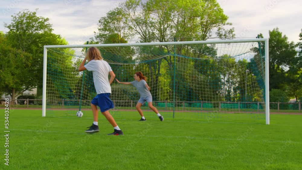 Slow motion shot of family playing soccer in park together. Happy parents and kids playing with ball in green meadow. Cheerful family enjoying summer outdoor activity Slow motion shot of family playing soccer in park together. Happy parents and kids playing with ball in green meadow. Cheerful family enjoying summer outdoor activity