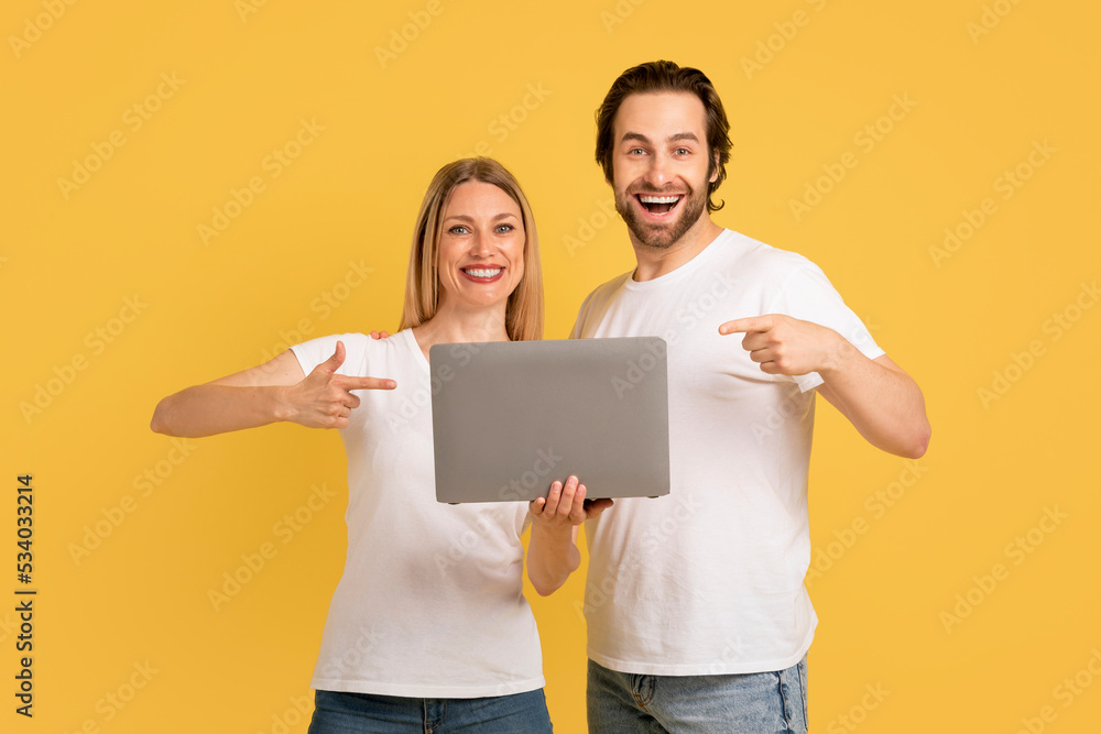 Glad young caucasian wife and husband in white t-shirts show fingers at laptop Glad young caucasian wife and husband in white t-shirts show fingers at laptop