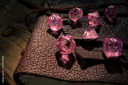 Pink transparent RPG dice on a leather-bound notebook