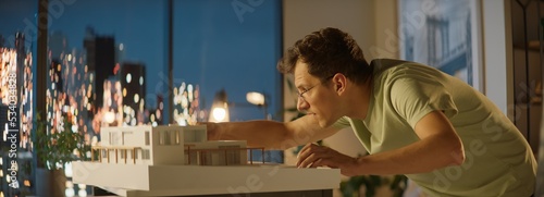 Portrait of Caucasian male architect or student working on a house project scale model late at home, preparing for presentation with a client