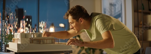 Portrait of Caucasian male architect or student working on a house project scale model late at home  preparing for presentation with a client