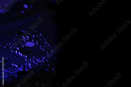 Electronic circuit board is illuminated in the dark with blue light and with free space for text on a black background. Abstract dark background with electronics concept