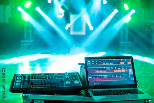 Highlighted deejay mixing with laptop on the stage with blue beams and lightshow