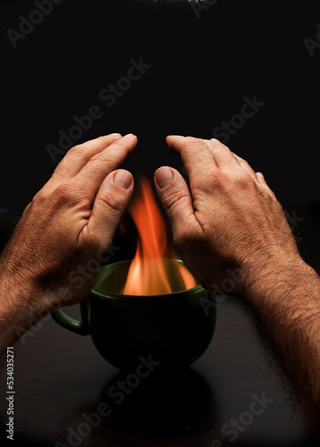 man's hands over cup with fire to warm up energy poverty 