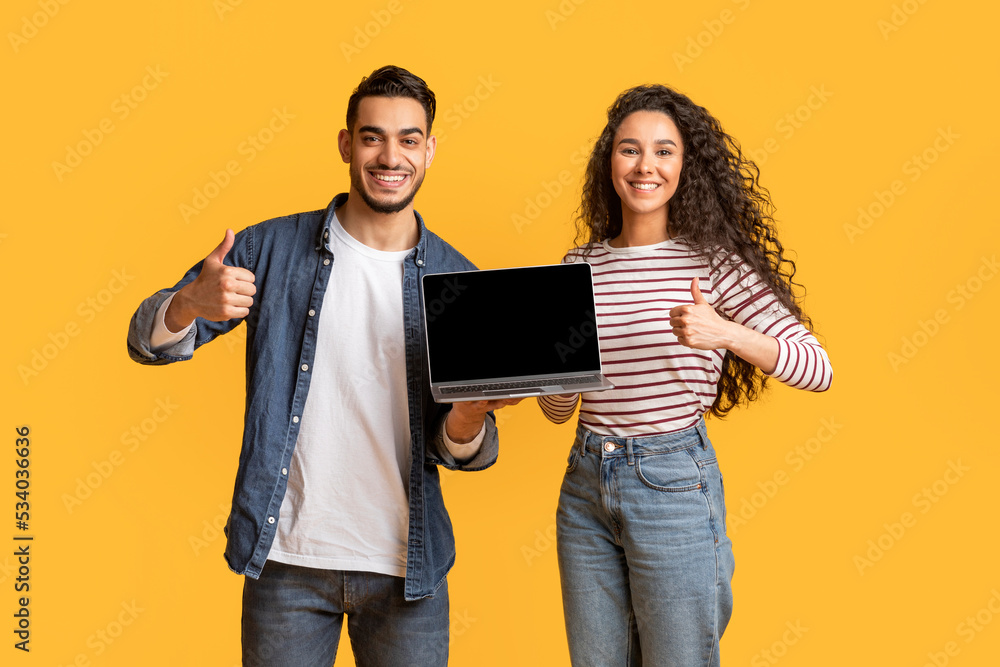 Fototapeta premium Smiling Arab Couple Holding Laptop With Black Screen And Showing Thumbs Up