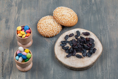 Dried raisin with bun and colorful candies on a wooden table