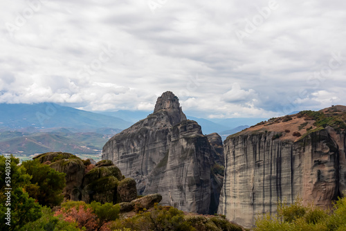 A dramatic view of the smooth rock pinnacles and mossy rocks of Meteora near tourist village of Kalambaka, Thessaly, Greece, Europe. Vista seen from Holy Trinity Monastery on cloudy dreamy day