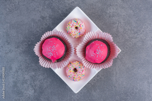 Chocolate balls with pink glaze and donuts on white plate