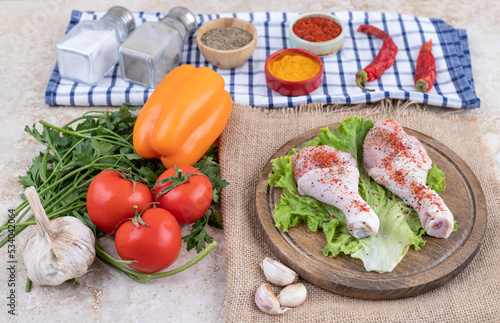 Uncooked chicken legs meat with vegetables on a wooden board