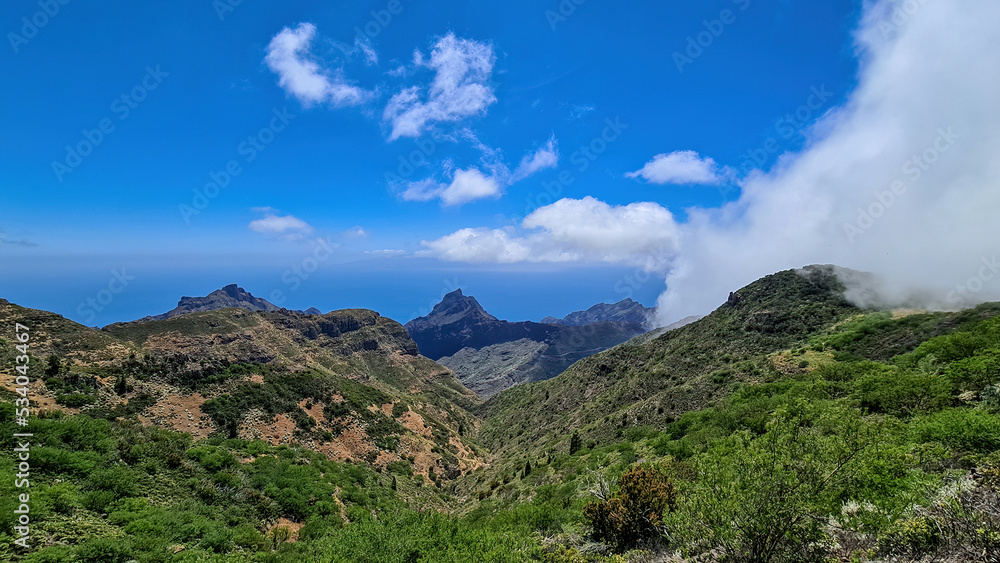 Fototapeta premium Panoramic view on the Teno mountain massif seen from summit Pico Verde, Tenerife, Canary Islands, Spain, Europe. Hiking trail between Masca and Santiago. Clouds over lush green hills. Tropical climate