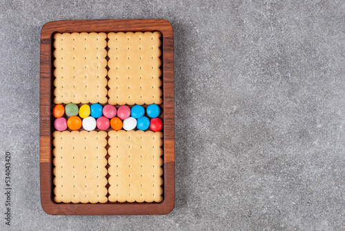 Biscuits and colorful candies on wooden plate