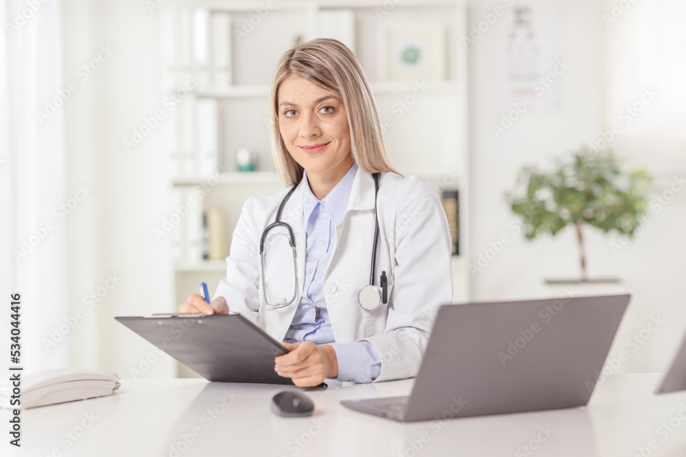 Young female doctor sitting in an office and writing a document at a desk Young female doctor sitting in an office and writing a document at a desk