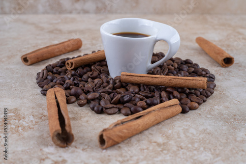 A cup of coffee, coffee beans and cinnamon sticks on marble background