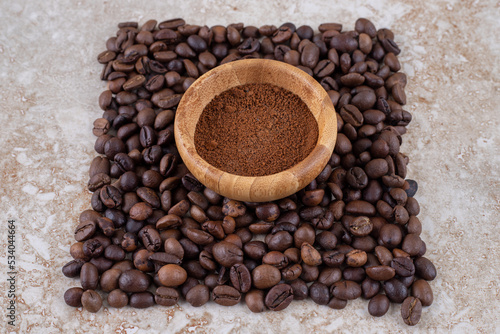 Small bowl with coffee powder surrounded with a small pile of coffee beans on marble background