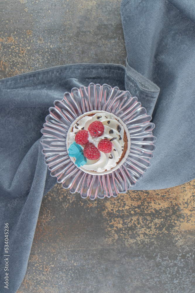 Cupcake on a glass pedestal wrapped with a piece of fabric on wooden background