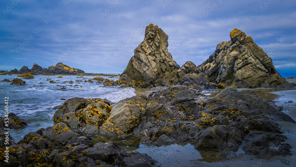 Massive volcanic rocks covered with seaweeds on Point St. George beach in Crescent City, California. Seascape with dramatic clouds at dusk on the deserted coastal footpath. 