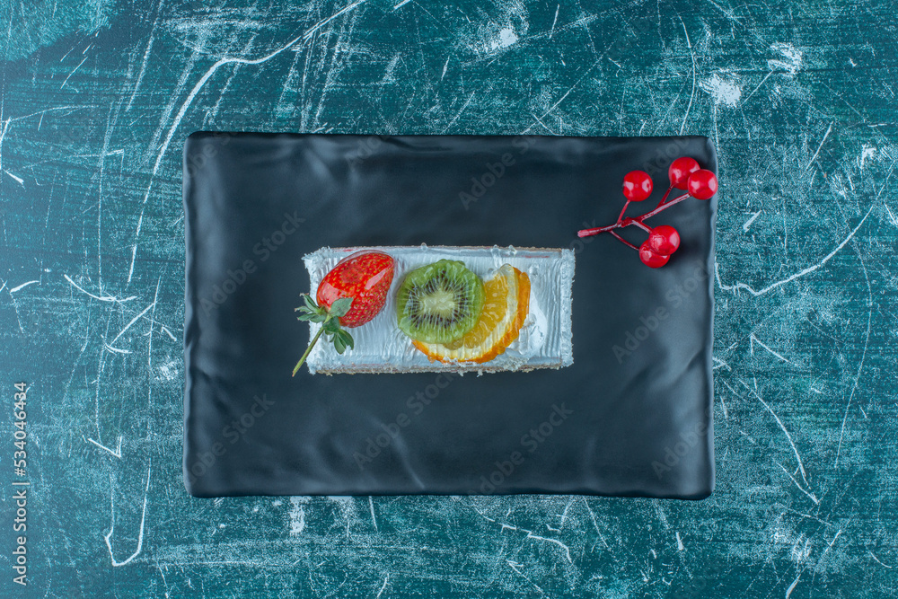 Obraz premium Cake slice with fruit topping on a platter on blue background