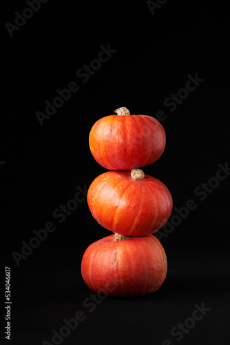 Three small bright orange pumpkins stacked on top of each other against the black background. Decoration for the Halloween holiday.