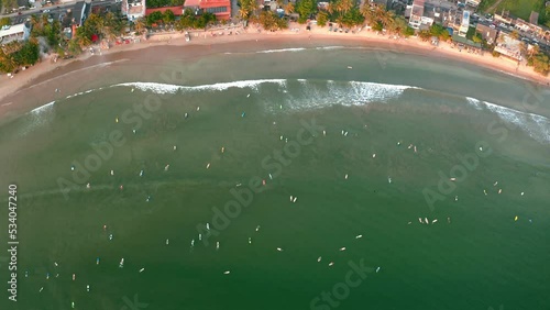 Flying drone video shot of dozens surfers floating on multicolors surfing boards at Dewata sandy beach harbor. Active vacation spending 4K top view footage. photo