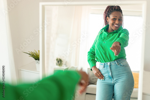 Self confident black woman pointing finger at her reflection in mirror, dancing and felling good, enjoying good mood photo
