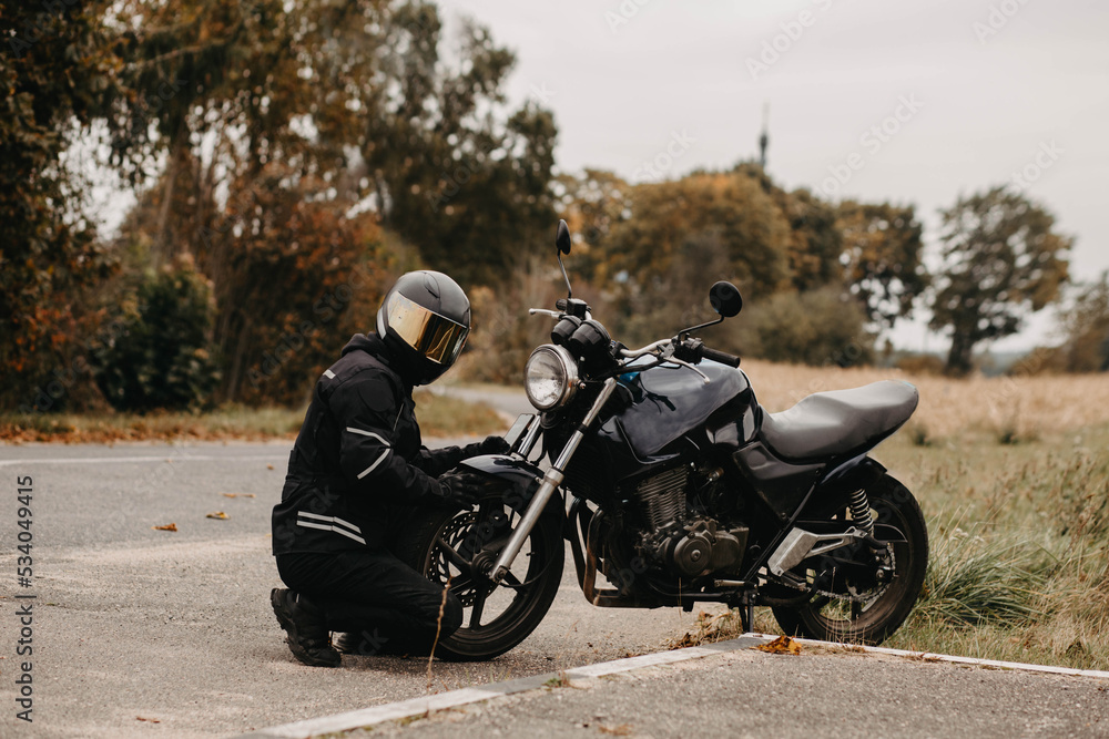 male motorcyclist in protective uniform and helmet with custom motorcycle cafe racer in autumn on the road.
