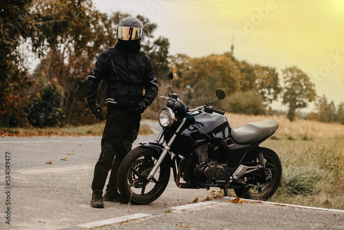 motorcyclist with motorcycle retro cafe racer on autumn road in uniform and helmet. the concept of the end of the motorcycle season.