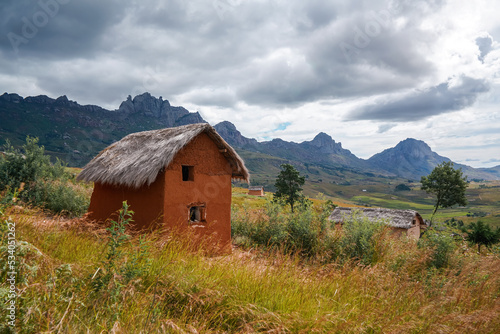 Typical landscape at Andringitra National Park, Madagascar on overcast day. Rocky mountains with rice fields under at distance, small clay house with stray roof in foreground