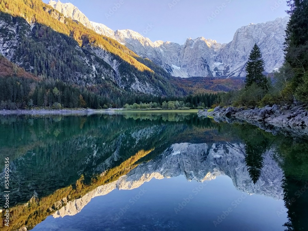 Reflection of forest and mountains in Lake Superiore in Fusine in autumn at sunset on the Julian Alps, Italy