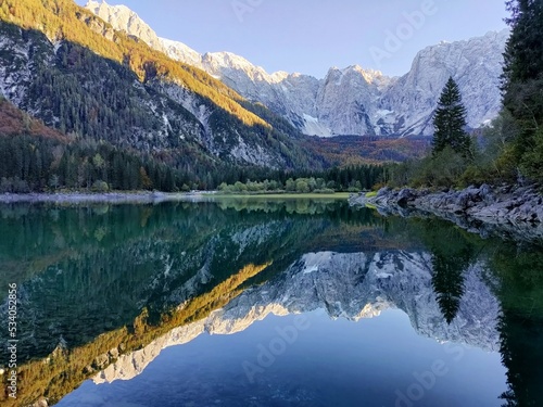 Reflection of forest and mountains in Lake Superiore in Fusine in autumn at sunset on the Julian Alps, Italy