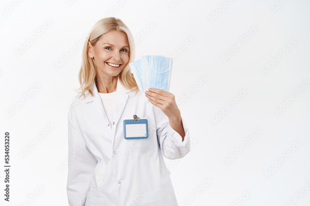 Happy beautiful woman doctor, shows medical face masks and smiles, promo of treating covid-19, wearing protective equipment from coronavirus, white background Happy beautiful woman doctor, shows medical face masks and smiles, promo of treating covid-19, wearing protective equipment from coronavirus, white background