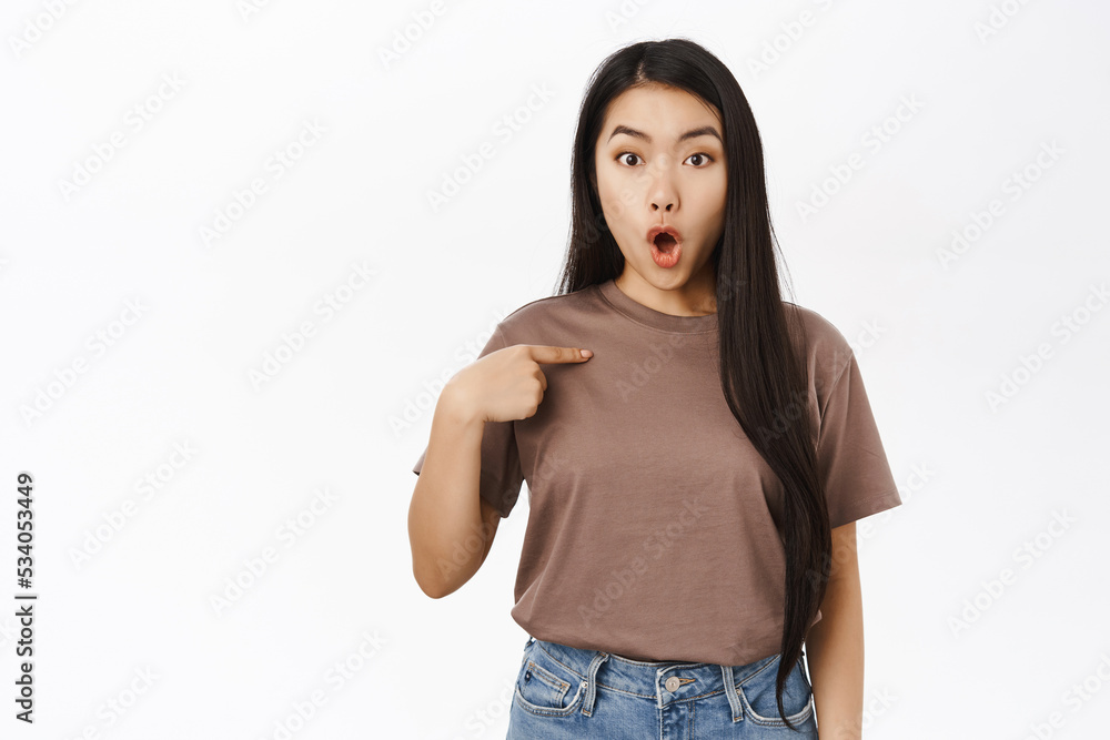 Surprised asian woman points at herself, gasping saying wow, looking impressed, standing over white studio background Surprised asian woman points at herself, gasping saying wow, looking impressed, standing over white studio background
