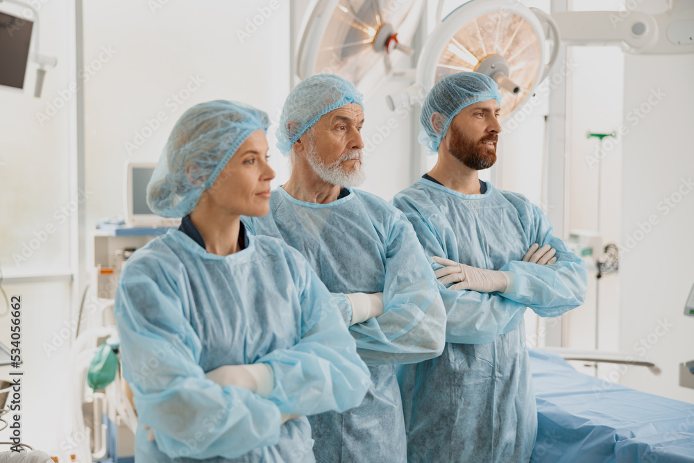 Team of professional surgeons with crossing hands standing in operating room before surgery