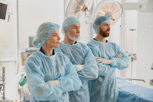 Team of professional surgeons with crossing hands standing in operating room before surgery