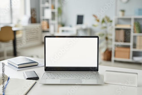 Background image of open laptop with white screen mock up at desk in minimal office interior white and grey tones, copy space