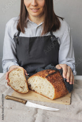 baker woman in a dark apron is cooking bread in the kitchen, a cook in a pastry shop is holding bread in her hands. fresh bread is on the cutting board. Baking and confectionery in a bakery or