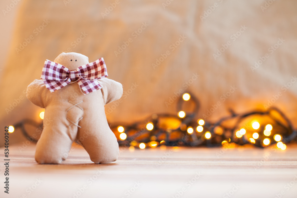 Fototapeta premium Handmade cloth gingerbread and blurred christmas lights in the background. Christmas decoration.