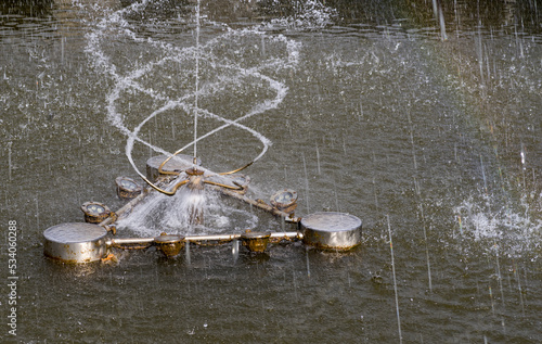 Fontanna w parkowym stawie , wystrzeliwująca spirale strumienie wody . Widoczna  miniaturowa tęcza . © Grzegorz