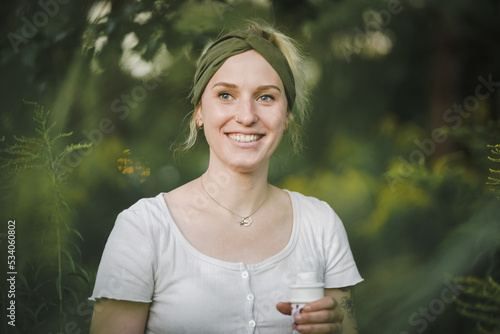 happy tattooed alternative & spiritual looking hipster woman smiling into the cam outside in a park with a green refreshed nature forest background
