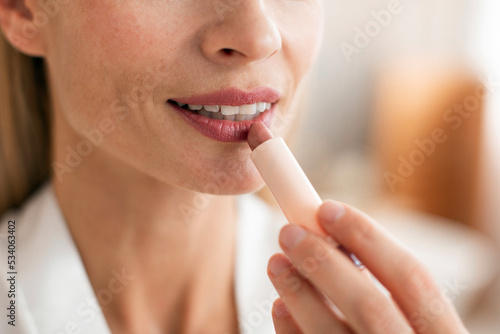 Middle aged woman applying nude lipstick on her lips  lovely mature lady using decorative cosmetics  closeup  cropped
