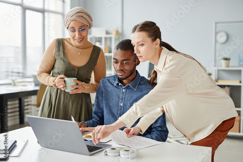 Obraz na plátně Diverse group of three business people using laptop together while discussing pr