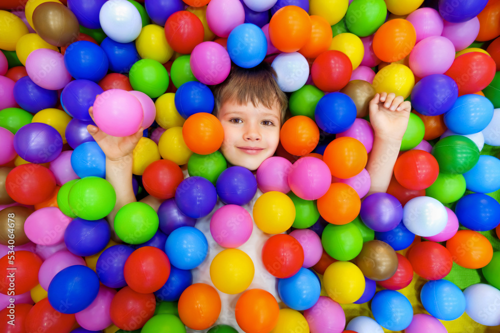Obraz premium Smile kid lying colorful plastic balls pool. Playroom kids ball pit. Colorful balls dry pool kindergarten playground child indoor play area. Caucasian boy indoor playground kids play zone or kids zone