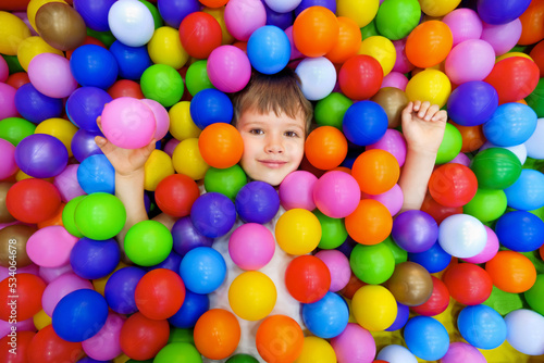 Smile kid lying colorful plastic balls pool. Playroom kids ball pit. Colorful balls dry pool kindergarten playground child indoor play area. Caucasian boy indoor playground kids play zone or kids zone